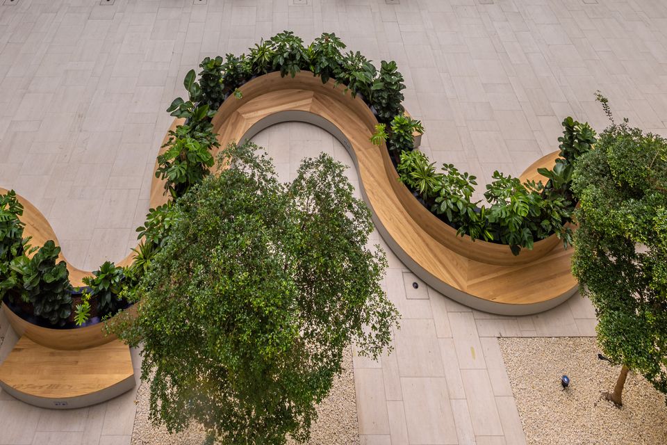 Organisch geschwungene Sitzbank mit integrierten Pflanzbeeten im Atrium, Kombination aus Holz und Grünflächen
