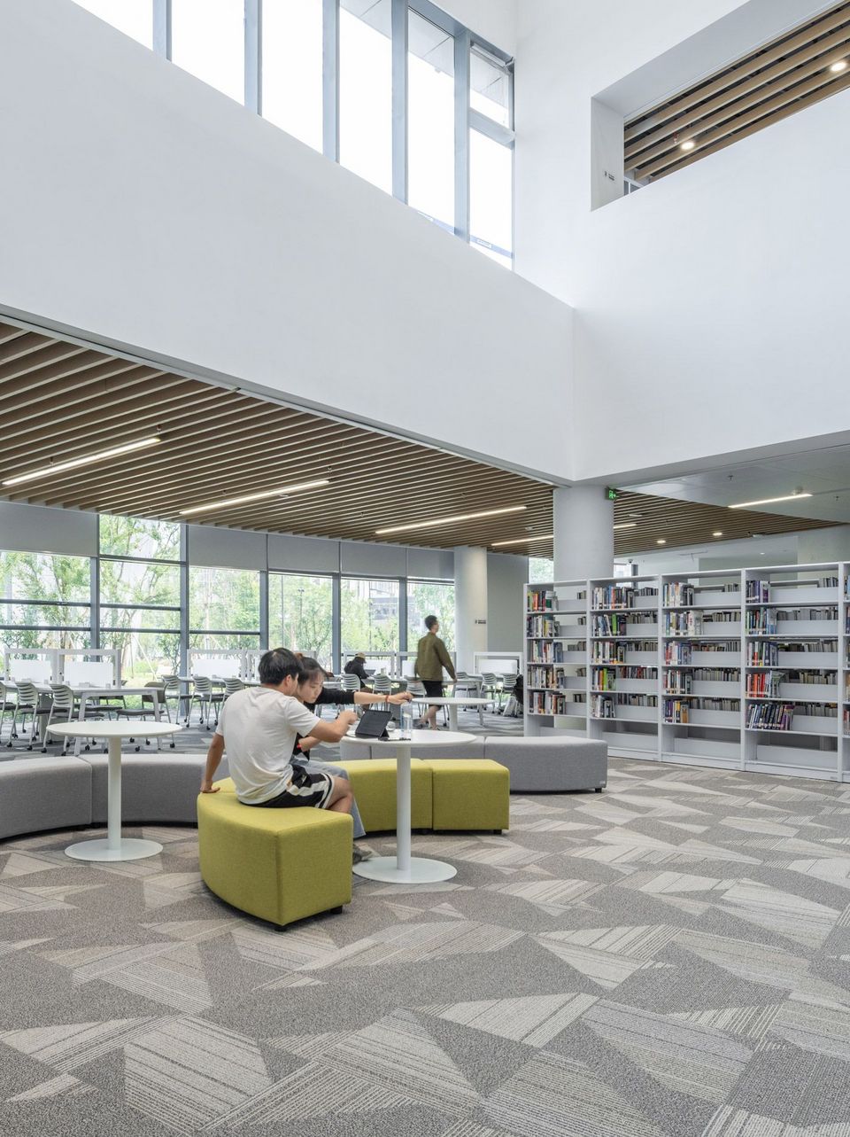 Innenaufnahme einer bibliotheksähnlichen Lernlandschaft mit hohen Fensterflächen, offenen Regalen und flexibel nutzbaren Sitzbereichen in einem lichtdurchfluteten Raumgefüge.