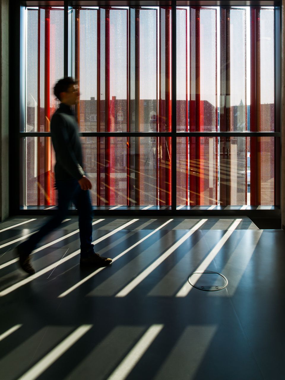 Innenaufnahme eines Flurbereichs mit Streiflicht, durchgehender Fensterfront und vertikaler Lamellenstruktur.