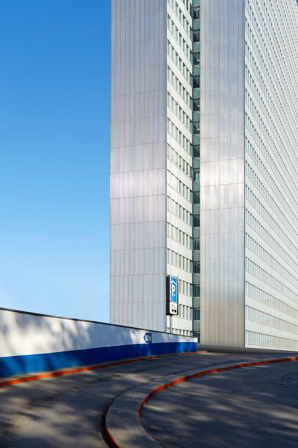 Detailansicht einer Hochhausfassade mit vertikalen Metallprofilen und Zufahrtsrampe, klare Linien und reflektierende Oberflächen
