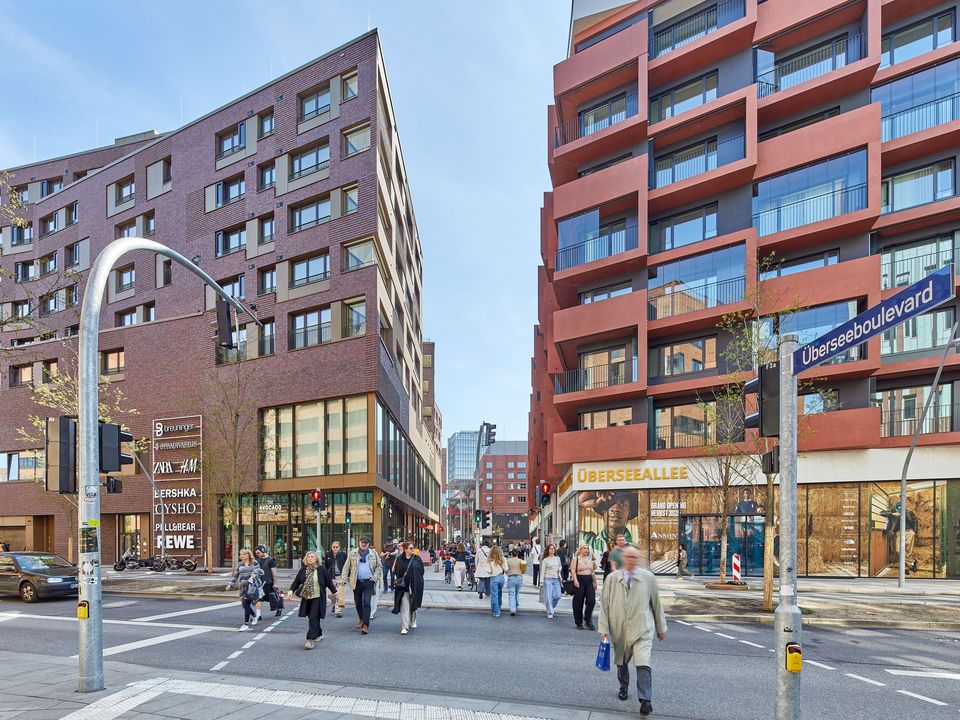 Innenaufnahme eines überdachten urbanen Atriums mit filigraner Dachstruktur, gastronomischen Angeboten und offenem Aufenthaltsbereich im Erdgeschoss.