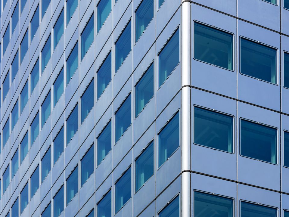 Detailansicht einer Hochhausfassade mit regelmäßigem Raster aus quadratischen Fenstern und silbernen Metallpaneelen