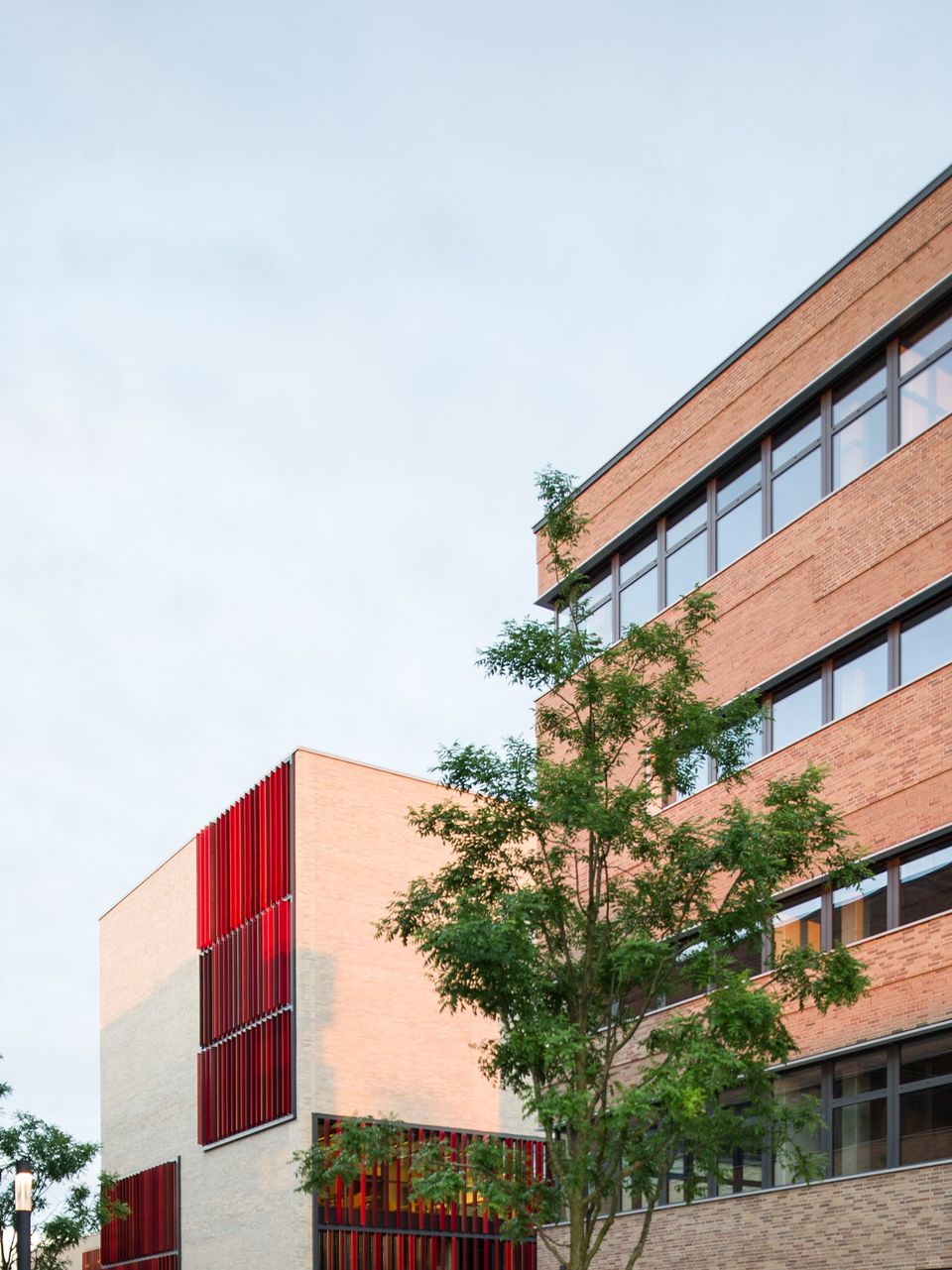 Außenaufnahme eines Campusgebäudes mit klarer Kubatur, großen Fensterflächen und roten Fassadenelementen.