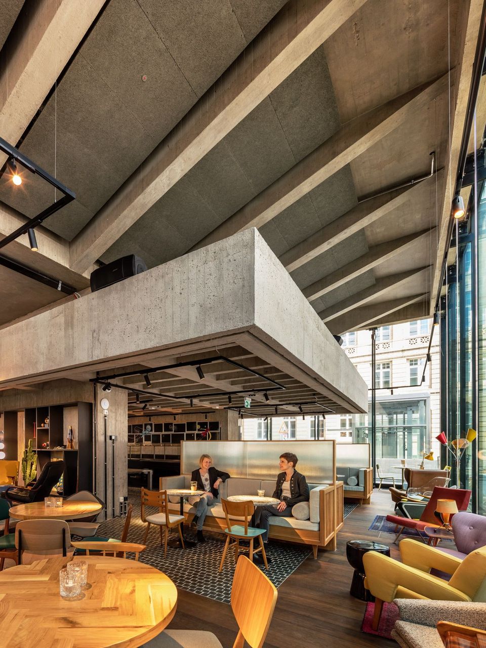 Innenraum mit markanter Betondecke und offenen Trägern, Lounge-Bereich mit Sitzgruppen und großen Glasfronten
