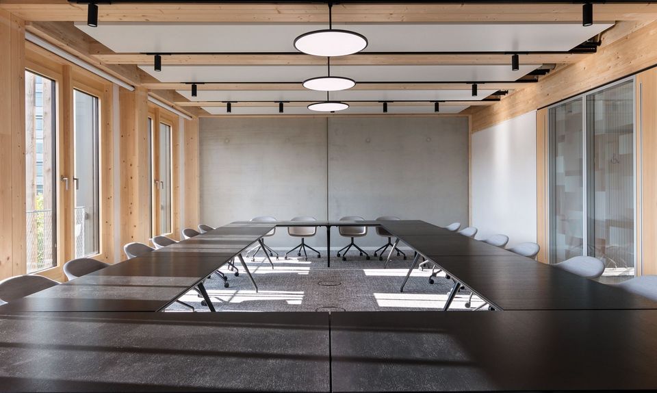 Konferenzraum mit großem U-förmigem Tisch, Holzverkleidung und runden Pendelleuchten, helle und funktionale Gestaltung