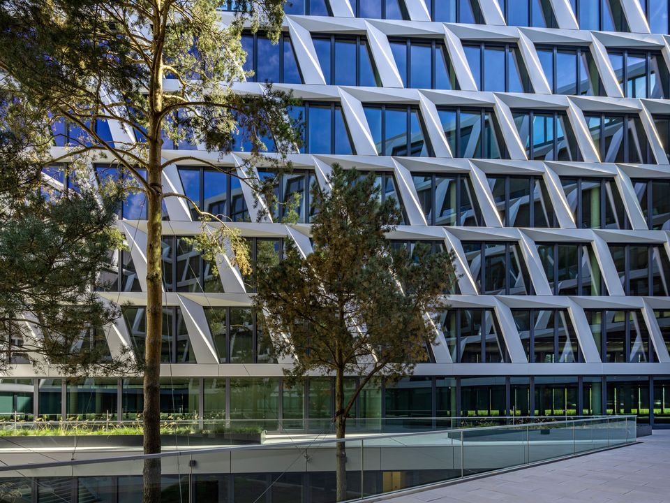 Außenaufnahme der strukturierten Bürofassade mit geometrischer Rahmenkonstruktion, großformatigen Fensterflächen und vorgelagertem Grünbereich.
