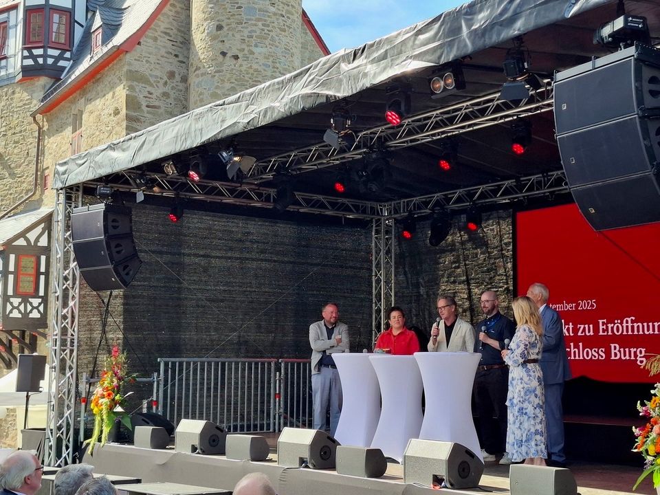 Außenaufnahme einer Bühnenveranstaltung im Burghof mit historischer Kulisse, moderner Eventtechnik und einer Gesprächsrunde auf der Bühne.