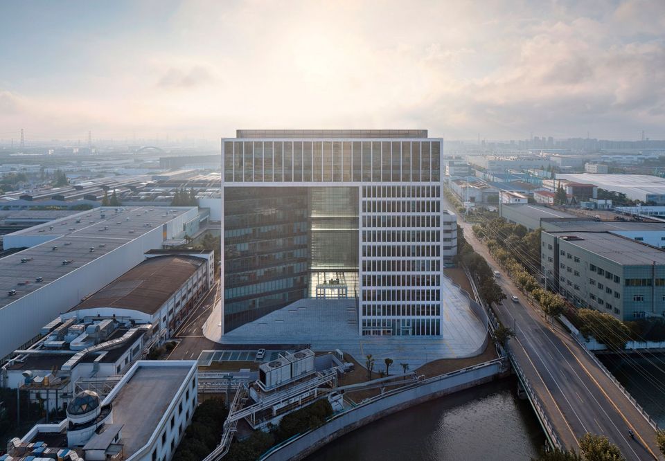 Weitwinkel-Außenaufnahme des SAIC Volkswagen Technical Centre mit großem Fassadenausschnitt, umlaufender Wasserführung und industriellem Stadtkontext, aufgenommen bei Sonnenaufgang.