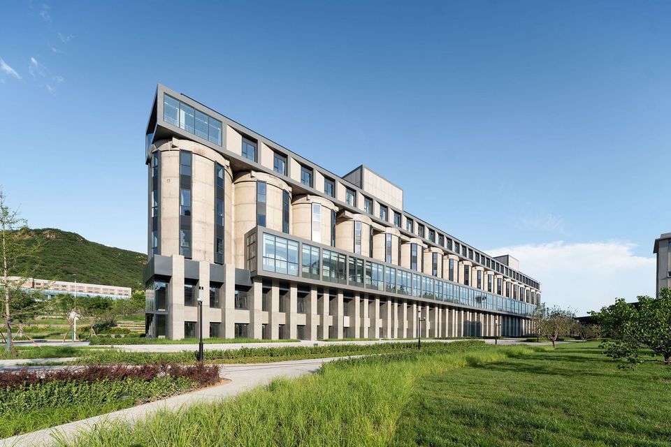 Langgestrecktes Gebäude mit integrierten Silos und moderner Glasfassade, industrielle Architektur in grüner Landschaft