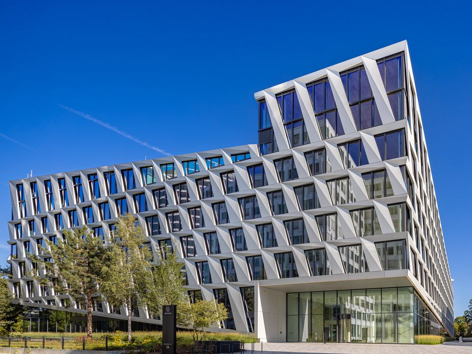 Seitenansicht eines Bürogebäudes mit dynamischer Fassadengeometrie und großen Glasflächen, eingebettet in Grünflächen