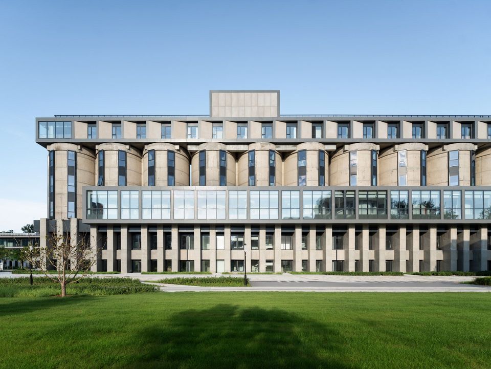 Weitwinkelaufnahme eines großmaßstäblichen Silogebäudes mit durchlaufender Fensterachse, ergänztem Dachaufbau und weitläufigem Grünraum davor.