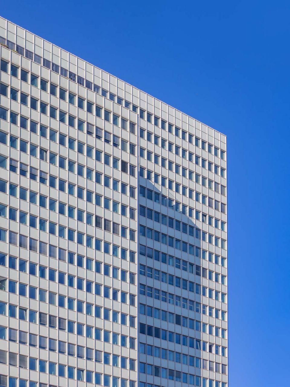 Detailaufnahme der Fassade eines Hochhauses mit eng rhythmisiertem Fenster- und Elementraster, das die vertikale Struktur und die klare Linienführung des Gebäudes betont.