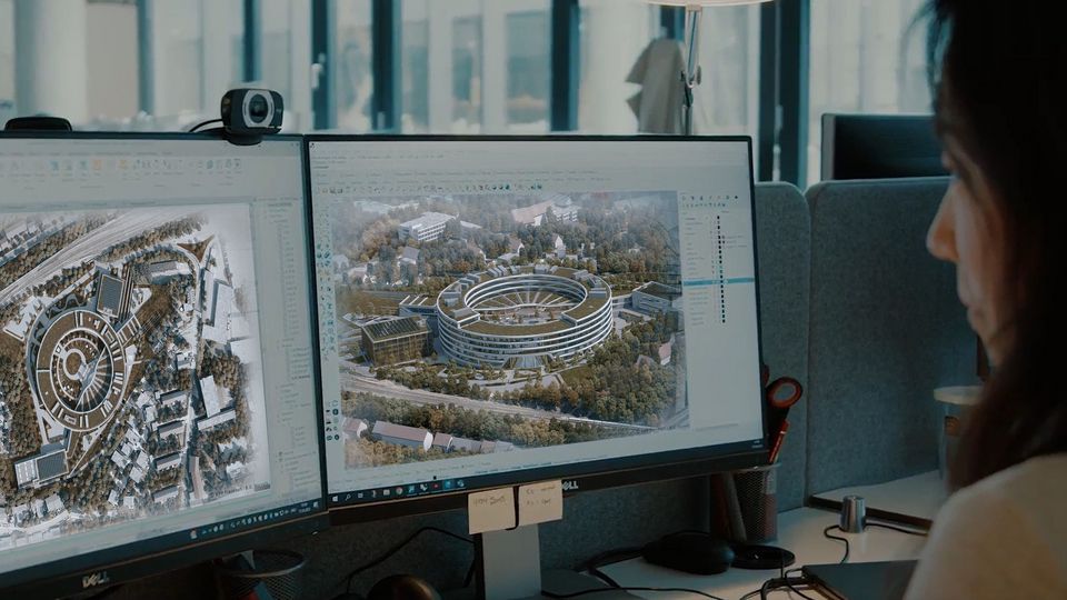 Innenaufnahme eines Büros mit drei Personen, die gemeinsam einen großformatigen Architekturplan betrachten, im Hintergrund gerahmte Projektvisualisierungen.