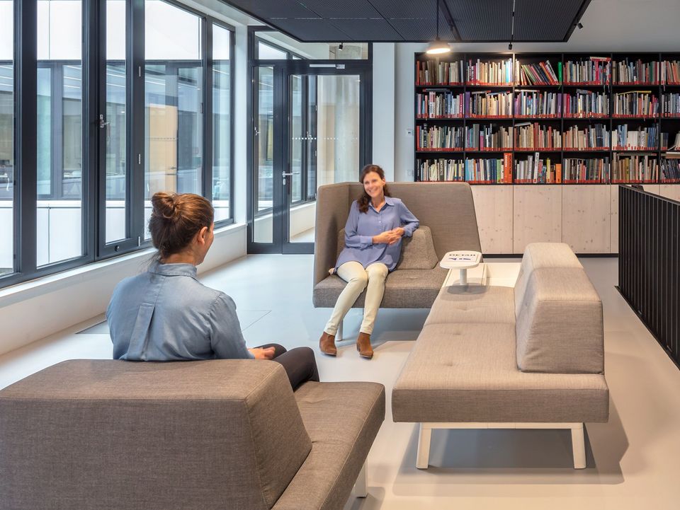 Innenaufnahme einer Sitzlounge mit modernen Polstermöbeln und angrenzender Bücherwand als Rückzugsbereich.