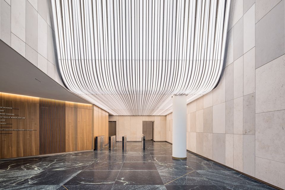  Innenaufnahme eines Foyers mit großformatigen Wandpaneelen, linearem Beleuchtungssystem und offener Wegeführung.