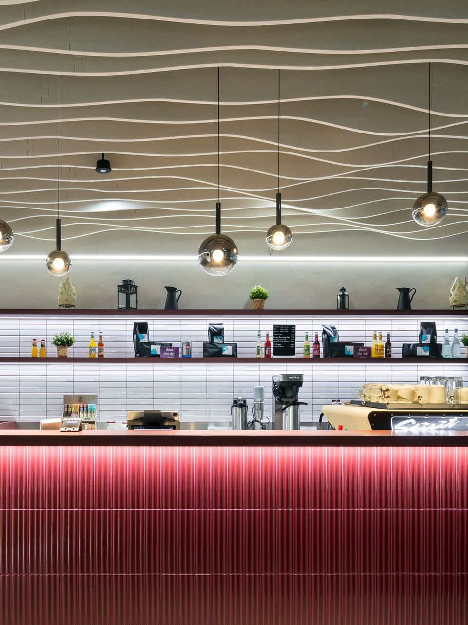 Barbereich mit roten Frontpaneelen, hängenden Kugelleuchten und Regalwand mit Getränken, moderne Innenarchitektur