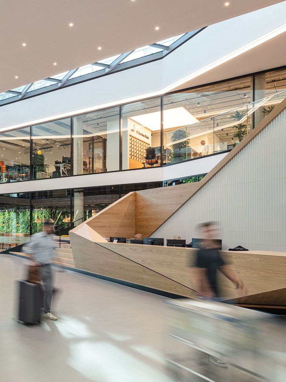 Großzügiges Atrium mit Holzverkleidung am Empfangstresen, Galerieebenen mit Glasfronten und Oberlicht für natürliche Belichtung
