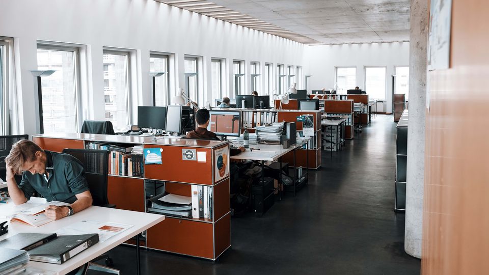 Innenaufnahme eines großzügigen Bürobereichs mit mehreren Arbeitsstationen, großen Fensteröffnungen, technischer Ausstattung und laufenden Projektarbeiten.