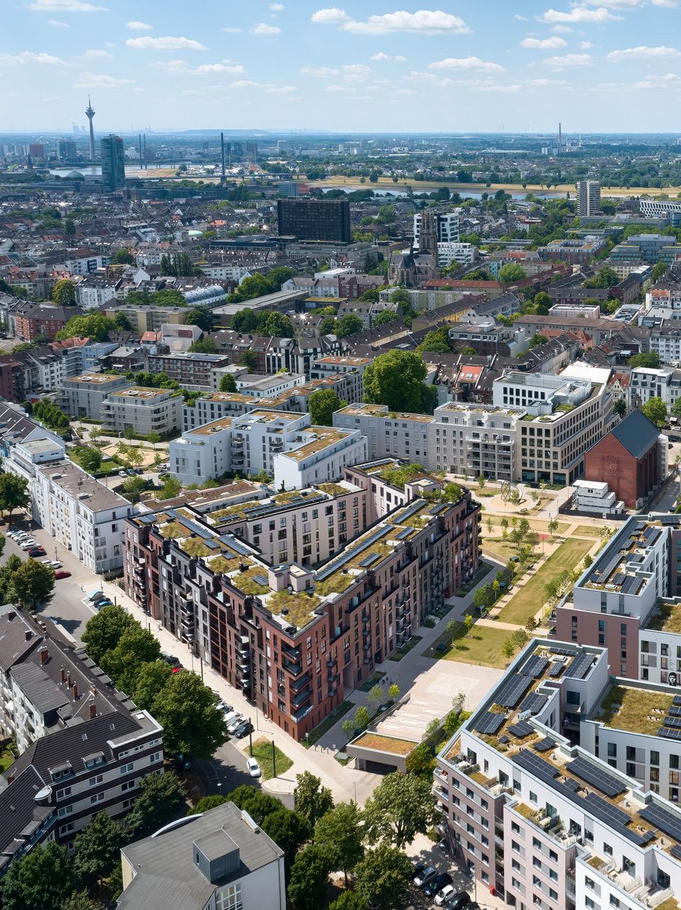 Luftaufnahme eines verdichteten Wohnquartiers mit geschlossenen Blockstrukturen, begrünten Dachflächen und zentralem Parkraum.