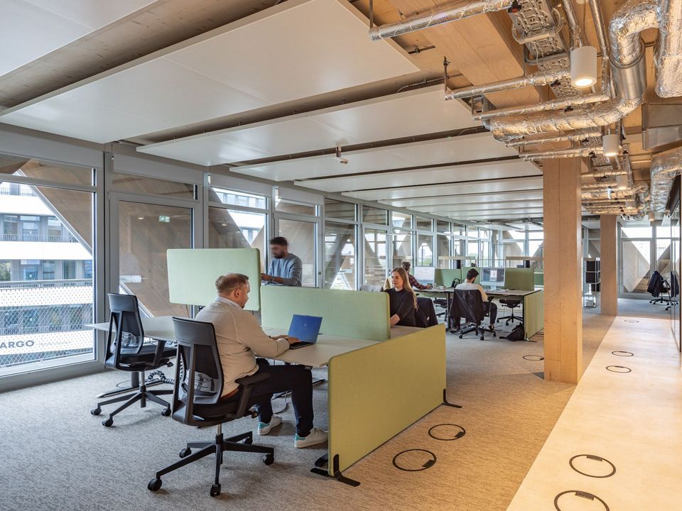 Offene Bürofläche mit modularen Arbeitsplätzen, sichtbarer Technikdecke und großen Glasfronten mit Dreiecksstruktur