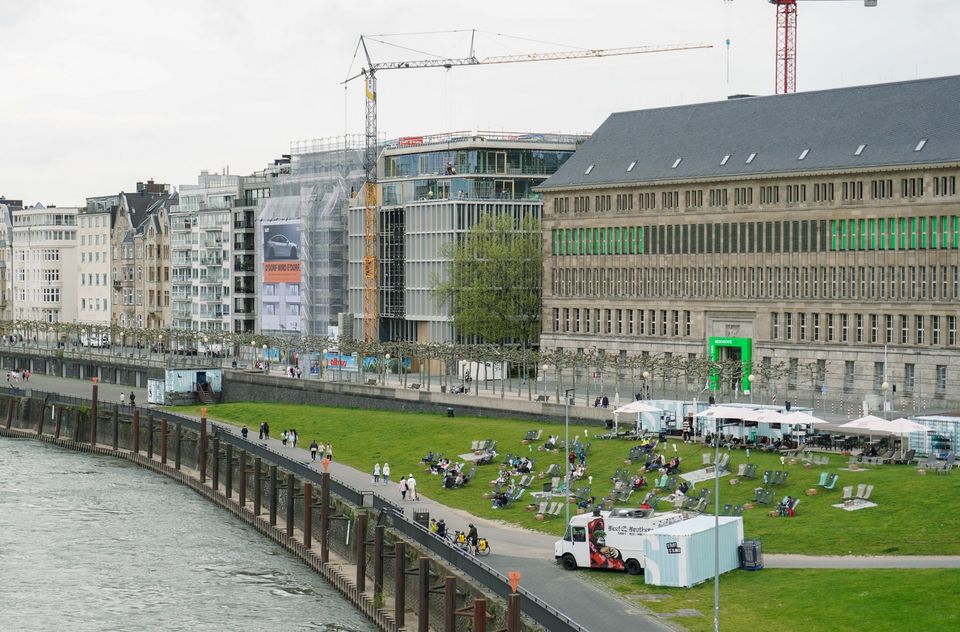 Außenaufnahme der Rheinfront mit im Bau befindlichem Neubau, Gerüststrukturen, Krananlagen und angrenzenden historischen Gebäuden neben der öffentlichen Uferwiese.