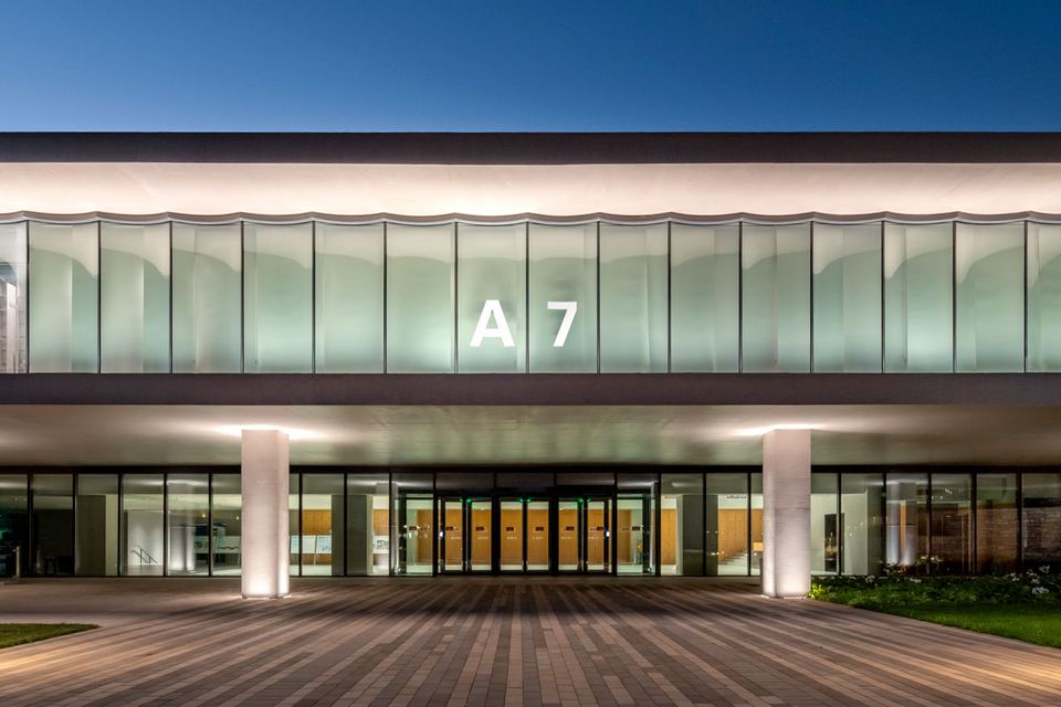 Eingangsbereich eines modernen Gebäudes mit durchgehender Glasfront und Beschriftung A7, klare Linien und abendliche Beleuchtung