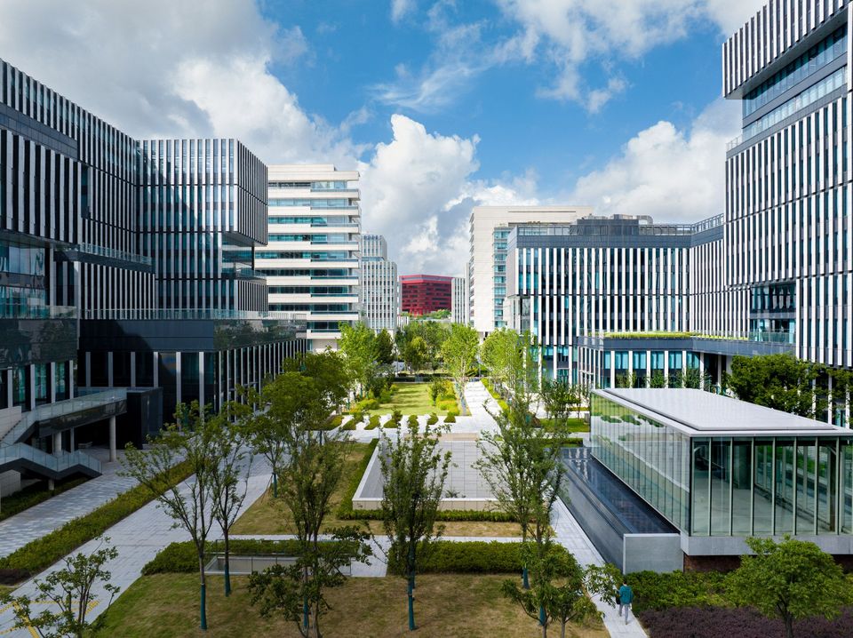 Luftaufnahme eines Campusensembles mit axial angeordneten Gebäudekörpern, zentralen Grünflächen, Wegen und umliegender urbaner Bebauung.