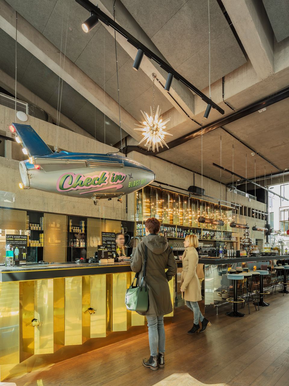 Barbereich mit goldfarbener Front, hängender Flugzeuginstallation und dekorativen Leuchten, industrielle Gestaltung mit Beton und Glas