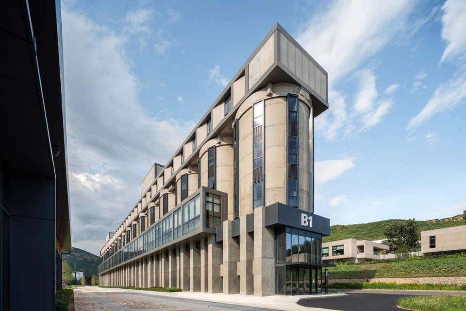 Außenaufnahme eines revitalisierten Silogebäudes mit aufgeständerten Baukörpern, vertikalen Fassadenöffnungen und angrenzenden Wegen im Campusbereich.