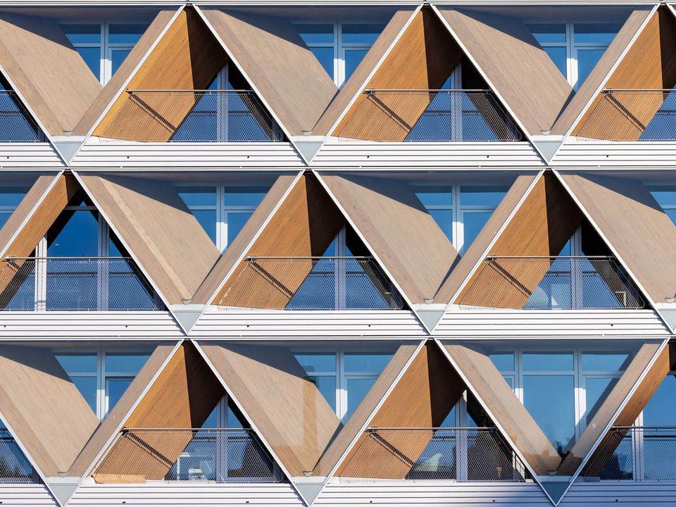 Detailansicht der Fassade mit dreieckigen Holz- und Metallmodulen, rhythmische Struktur und integrierte Balkone