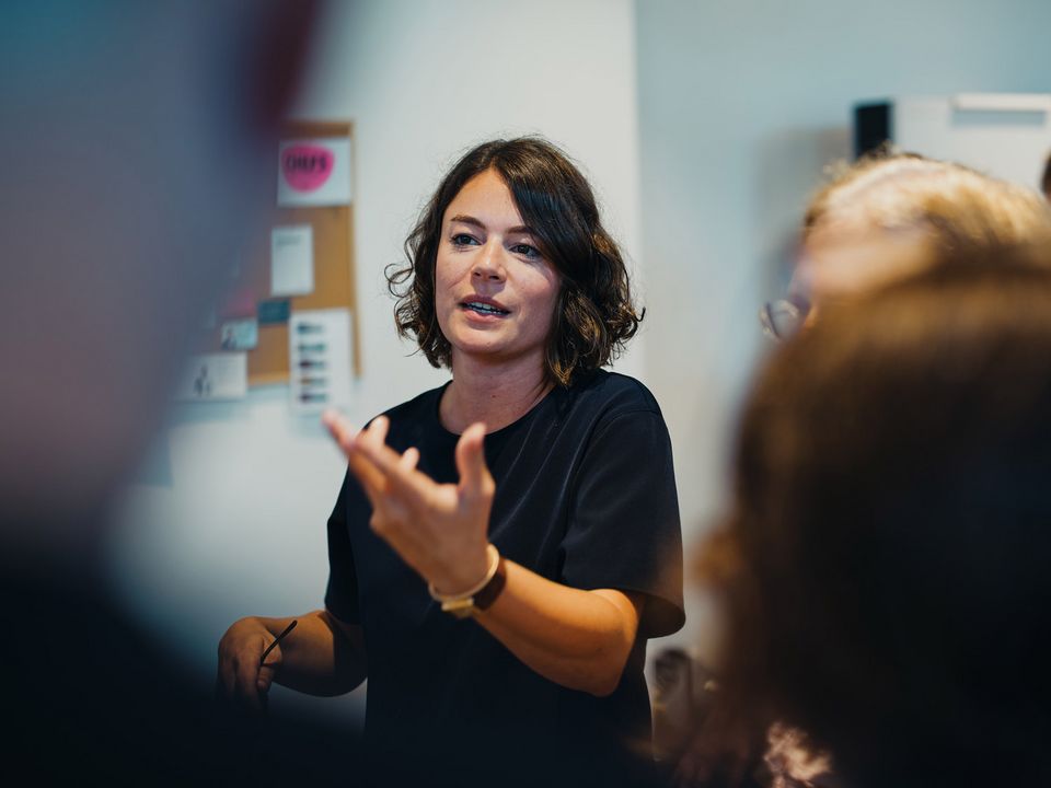 Aufnahme einer Workshop-Situation in einem kreativen Arbeitsumfeld. Eine Person erklärt Inhalte vor einer Gruppe.