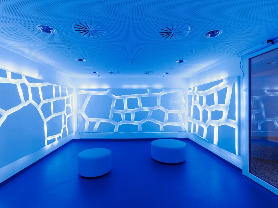 Therapieraum mit blauer Lichtinstallation und organisch geformten Wandmustern, futuristische Gestaltung mit runden Sitzhockern