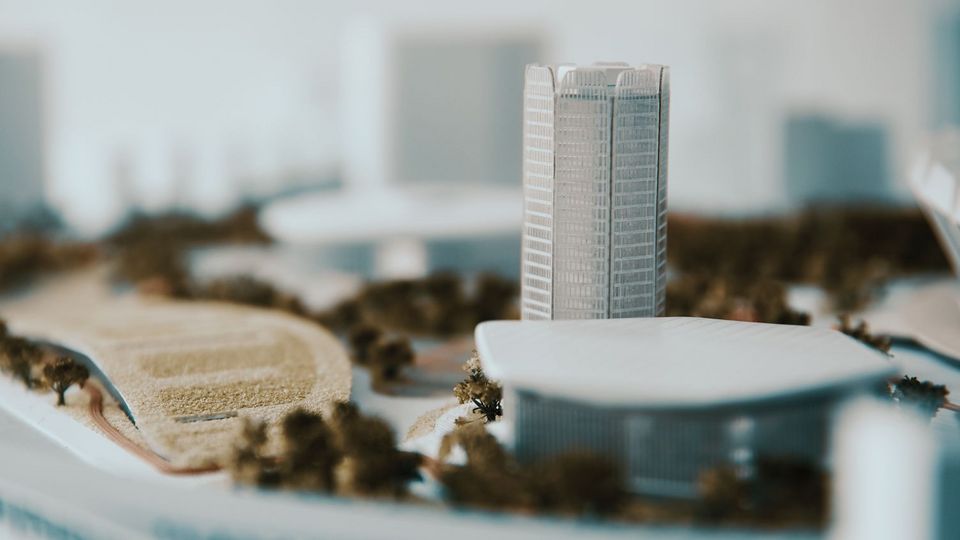 Detailaufnahme eines architektonischen Stadtmodells mit einem hochliegenden Turmvolumen, umliegenden Gebäudestrukturen, modellierten Landschaftsbereichen und Wegen.