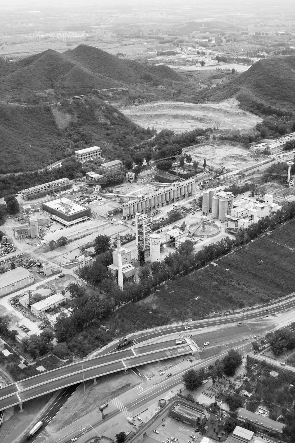 Historische Luftaufnahme eines Industrieareals mit Silos und Produktionsanlagen, eingebettet in hügelige Landschaft