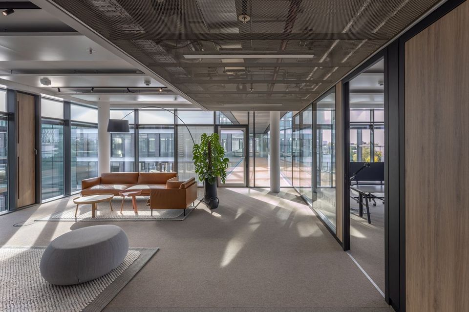 Innenraum eines Büros mit Glaswänden, Lounge-Bereich mit Ledersofa und Designmöbeln, lichtdurchflutete Arbeitsumgebung