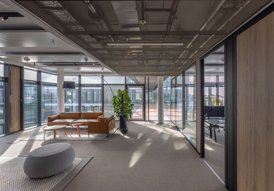 Interior of an office with glass walls, lounge area with leather sofa and designer furniture, light-filled working environment