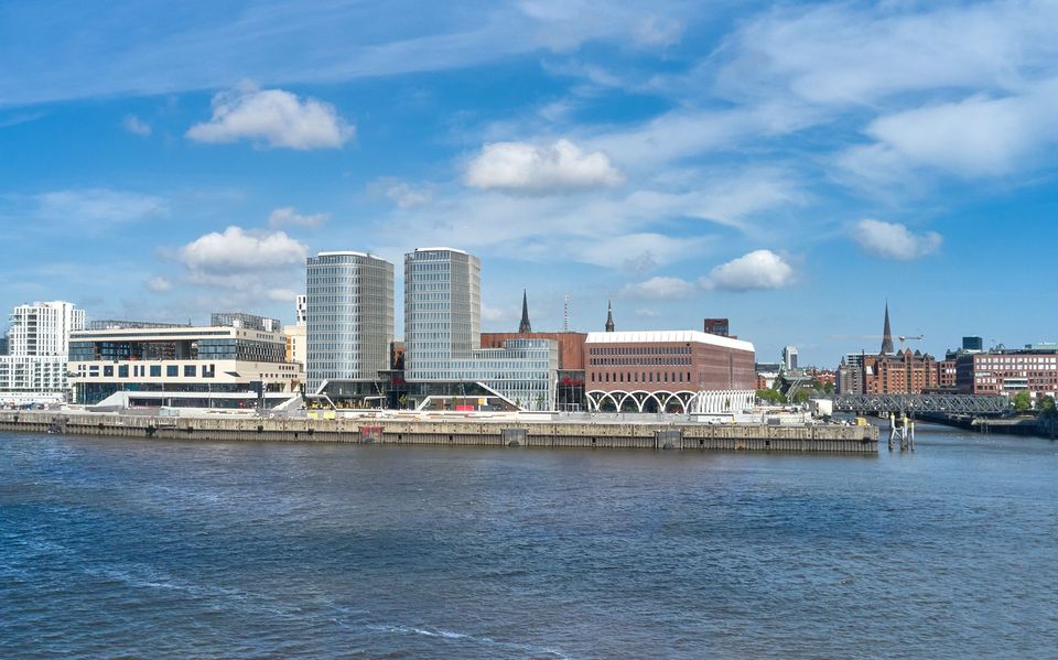 Panoramaaufnahme des Überseequartiers vom Wasser aus mit Hochhausstrukturen, Ziegelfassaden, Promenade und umliegender Stadtlandschaft.