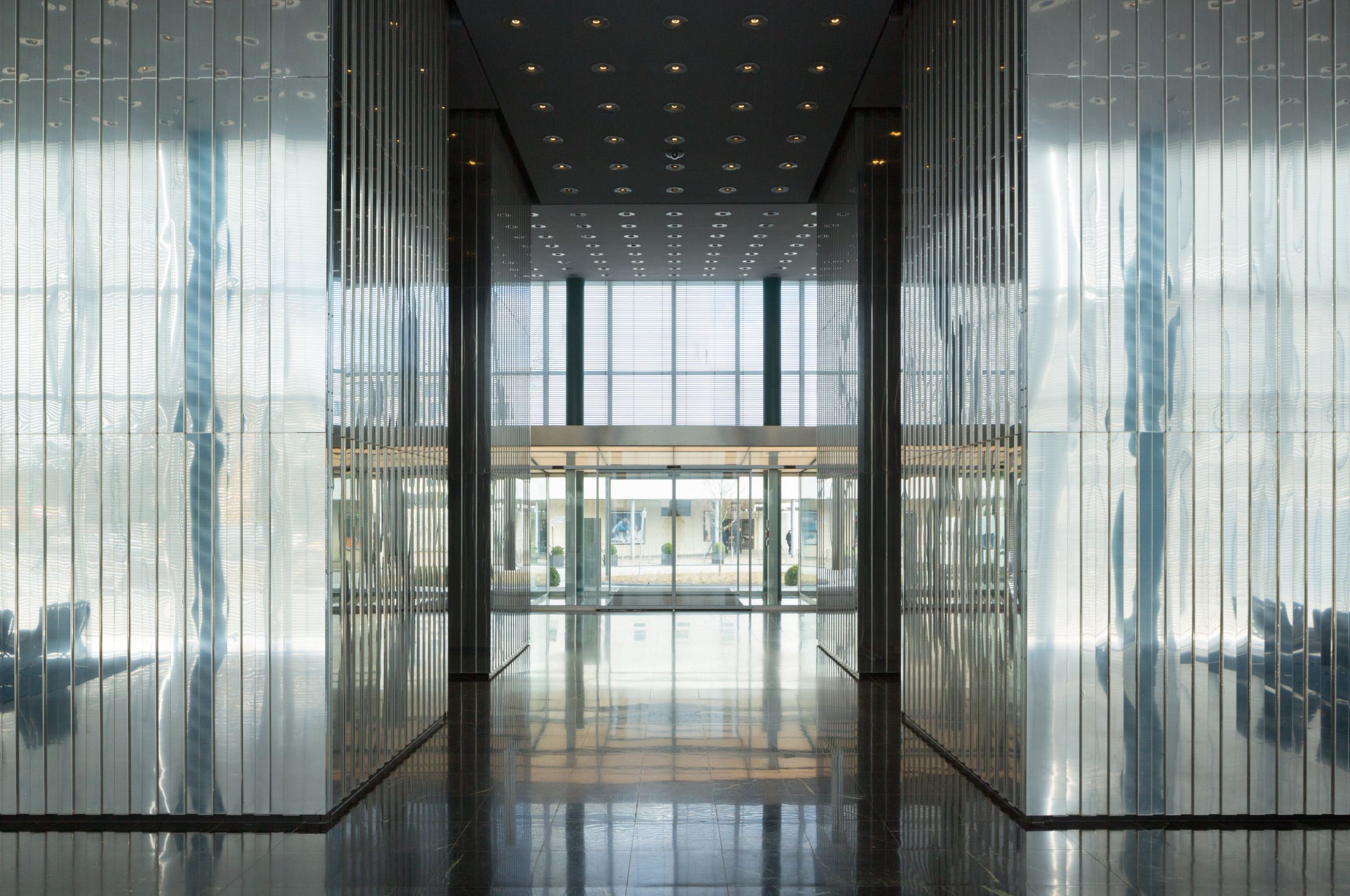 Helles, modernes Lobbyfoyer mit Glaswänden, reflektierendem Boden und großer Fensterfront im Hintergrund